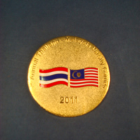 เหรียญรางวัลที่ระลึก การแข่งขันกีฬามิตรภาพระหว่างสถาบันอุดมศึกษาไทย – มาเลเซีย ครั้งที่ 4 ระหว่างวันที่ 20 - 24 กรกฎาคม 2554 ณ มหาวิทยาลัยแม่ฟ้าหลวง  (ด้านหลังเป็นธงชาติไทย และธงชาติมาเลเซีย และปีที่จัดการแข่งขัน)